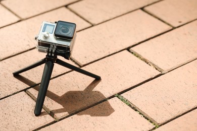 Photo of Modern action camera with tripod on pavement outdoors, space for text