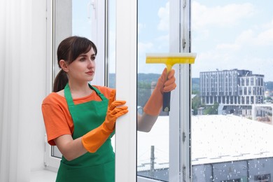 Young housewife with squeegee cleaning window indoors