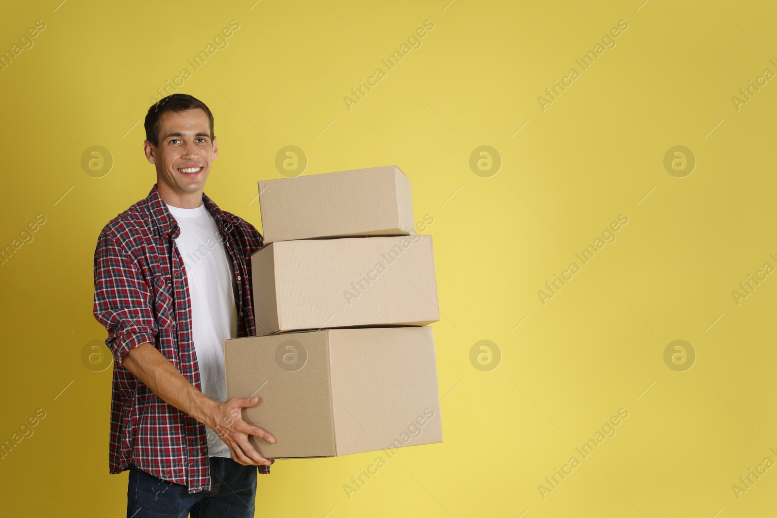 Photo of Moving into new house. Man with cardboard boxes on yellow background, space for text