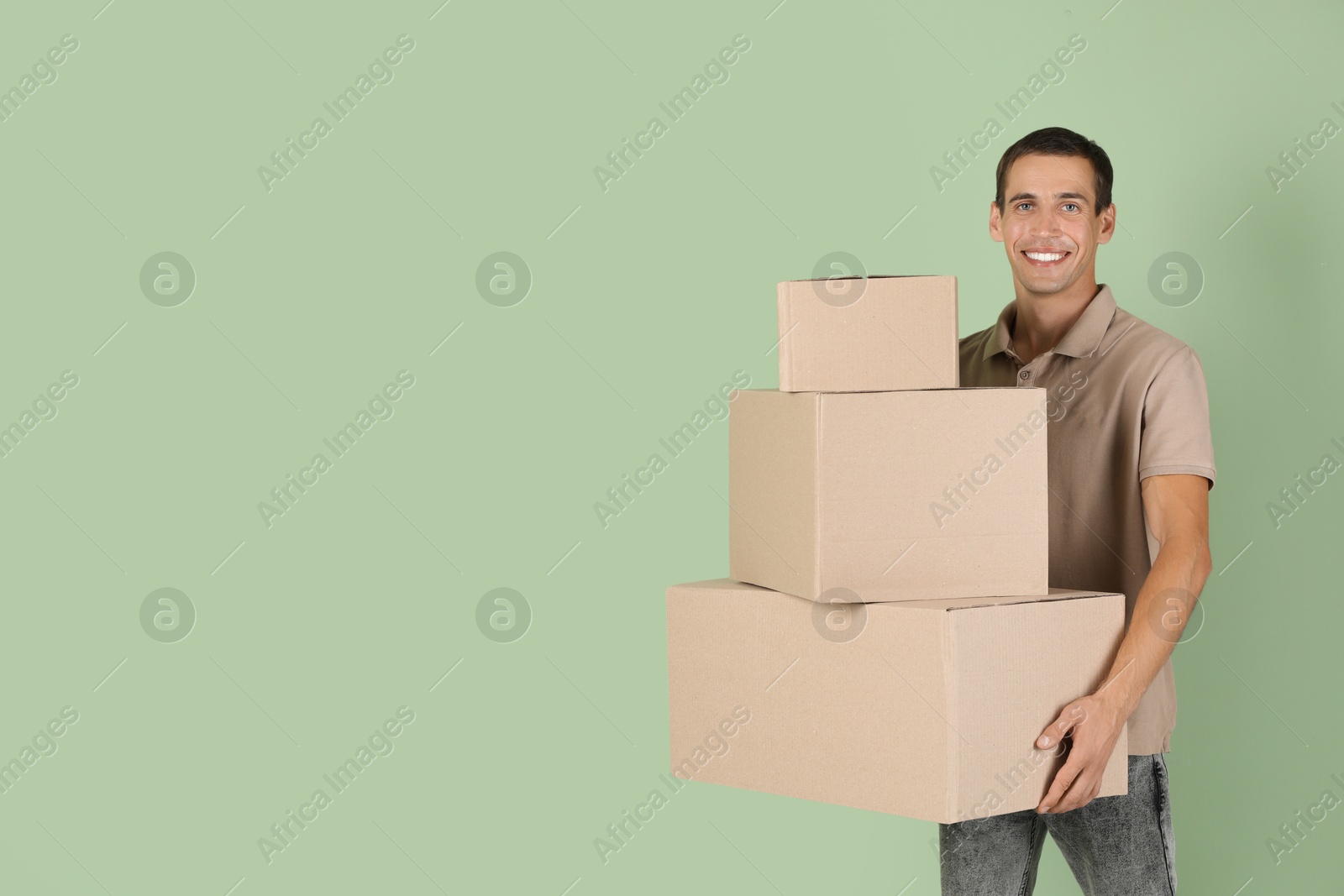 Photo of Moving into new house. Man with cardboard boxes on light green background, space for text