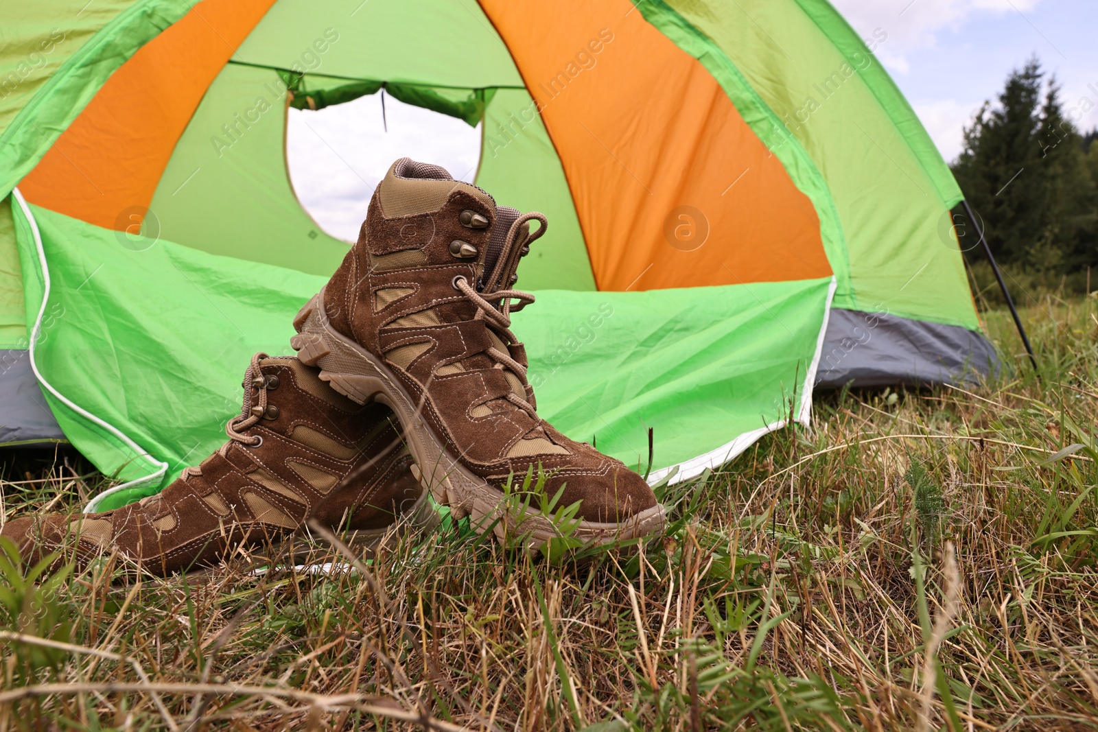 Photo of Trekking shoes and camping tent on green grass outdoors