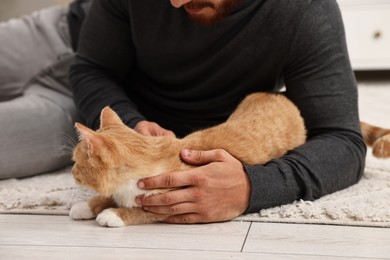 Man petting cute ginger cat on floor at home, closeup