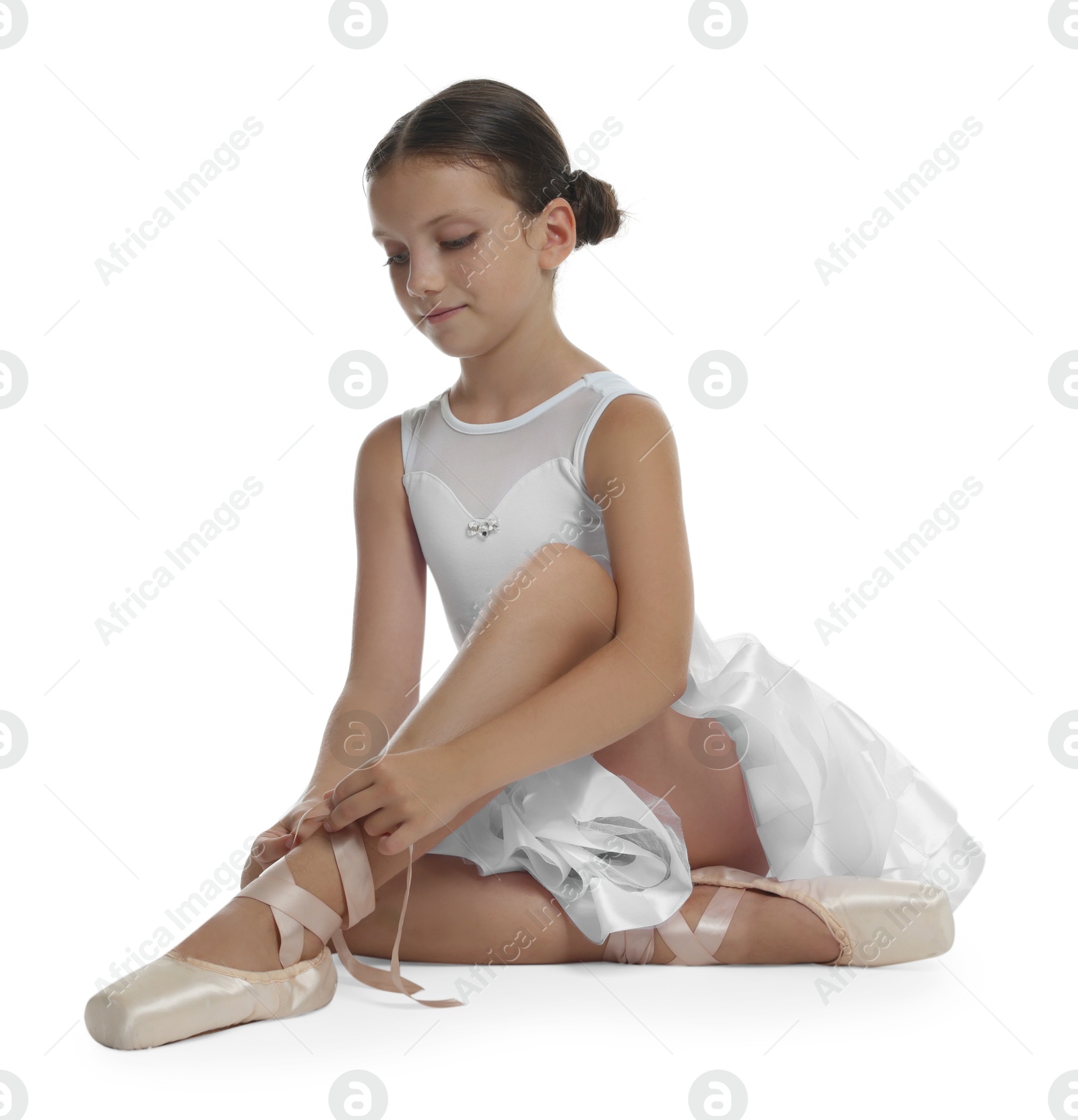 Photo of Little ballerina tying pointe shoes on white background