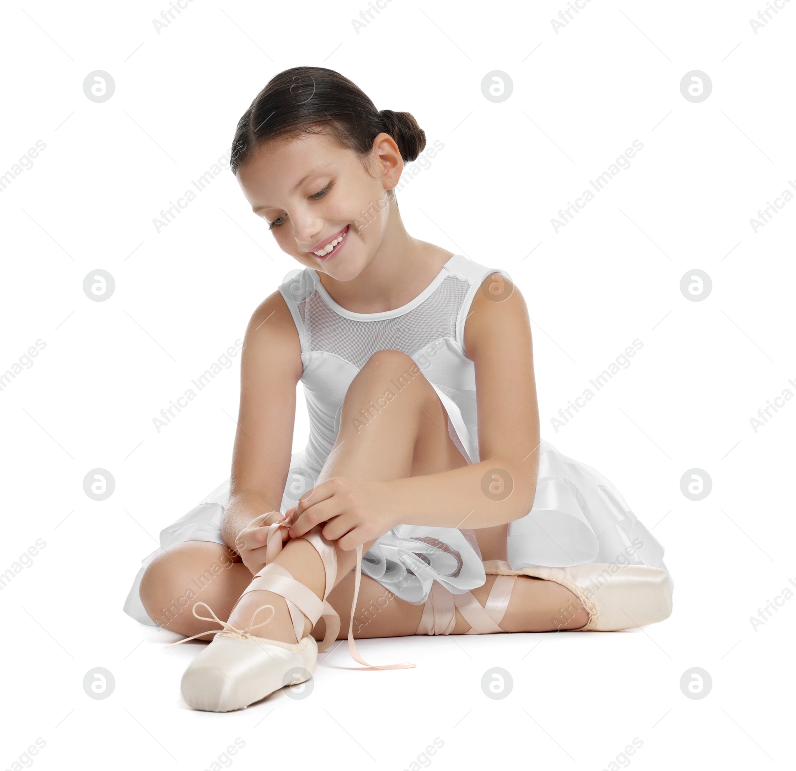 Photo of Little ballerina tying pointe shoes on white background