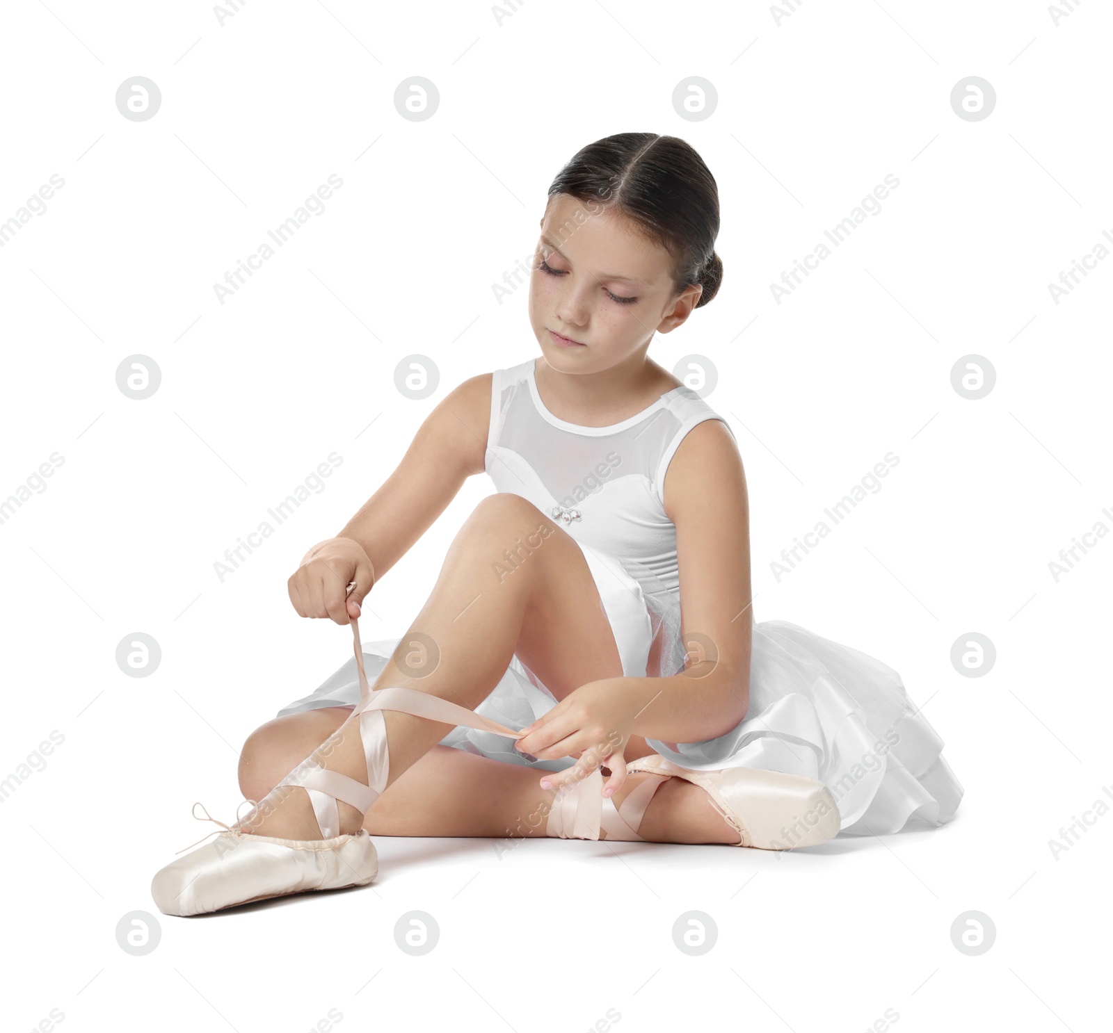 Photo of Little ballerina tying pointe shoes on white background