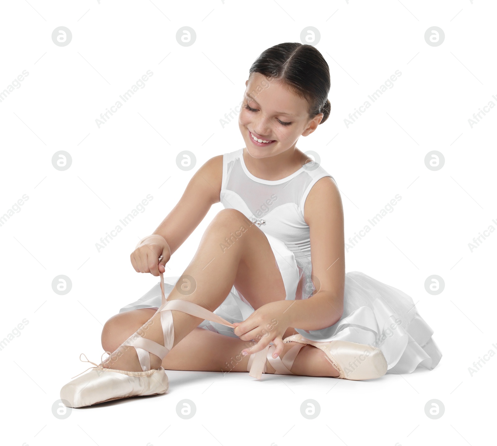 Photo of Little ballerina tying pointe shoes on white background