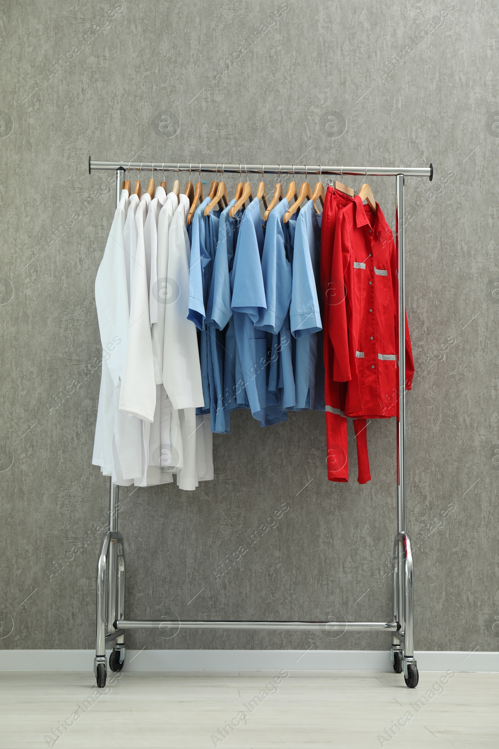 Photo of Different medical workers' uniforms on clothing rack against grey background