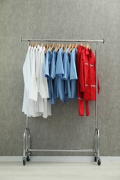 Photo of Different medical workers' uniforms on clothing rack against grey background