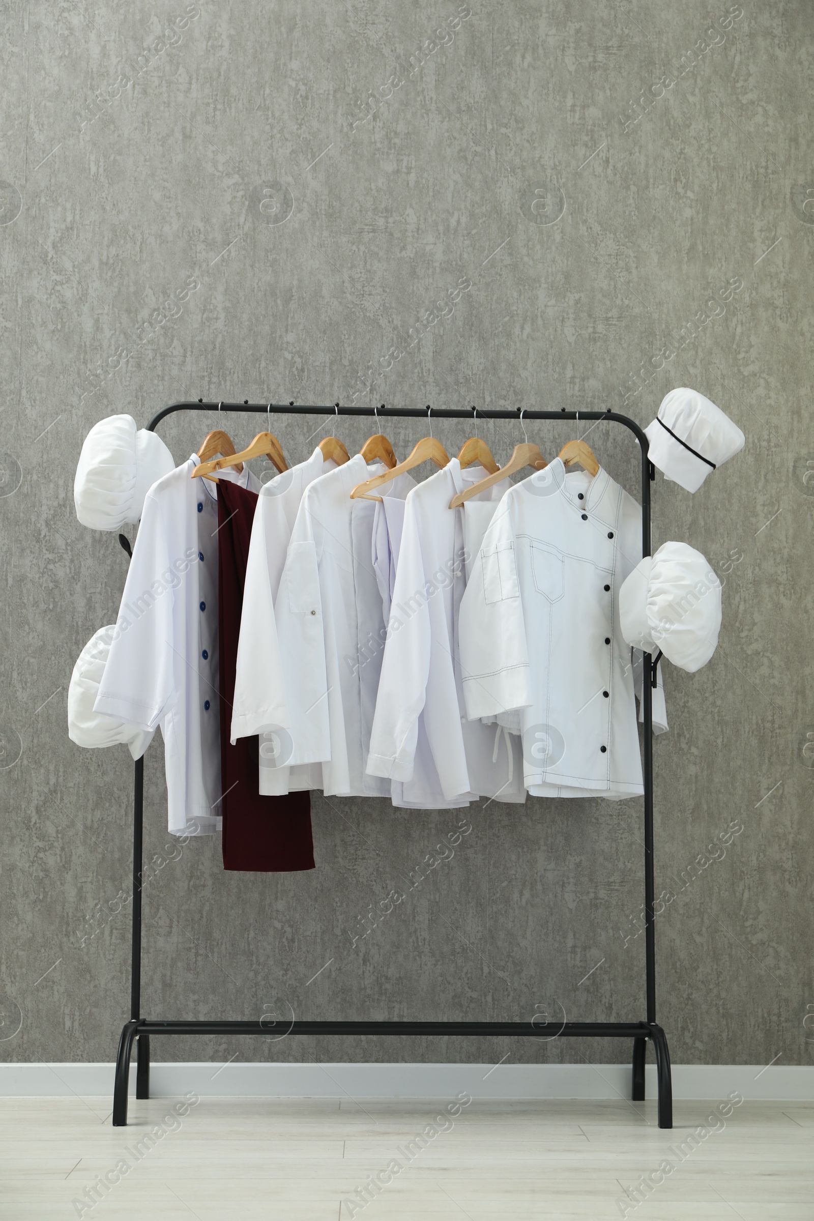 Photo of Chefs' uniforms on clothing rack near grey wall indoors