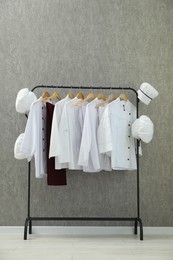 Chefs' uniforms on clothing rack near grey wall indoors