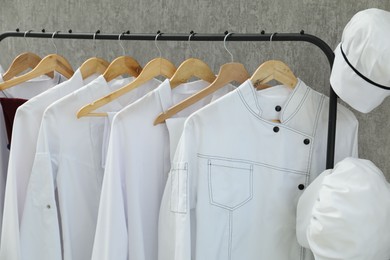 Photo of Chefs' uniforms on clothing rack against grey background, closeup