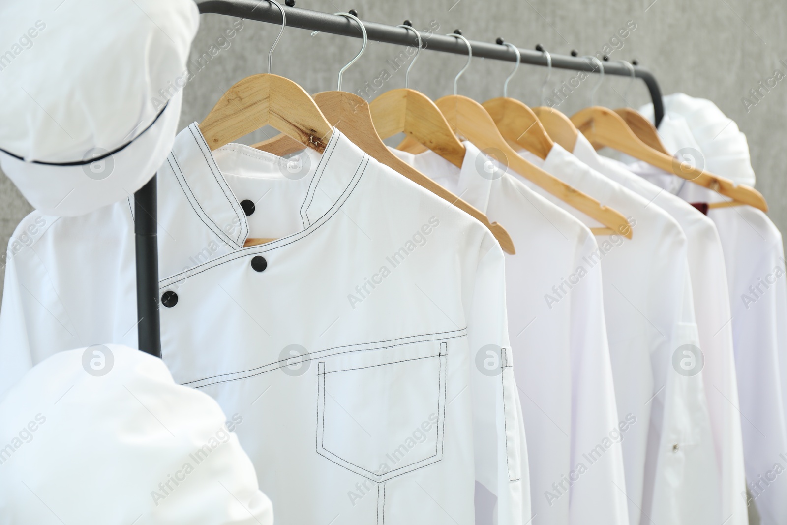 Photo of Chefs' uniforms on clothing rack against grey background, closeup