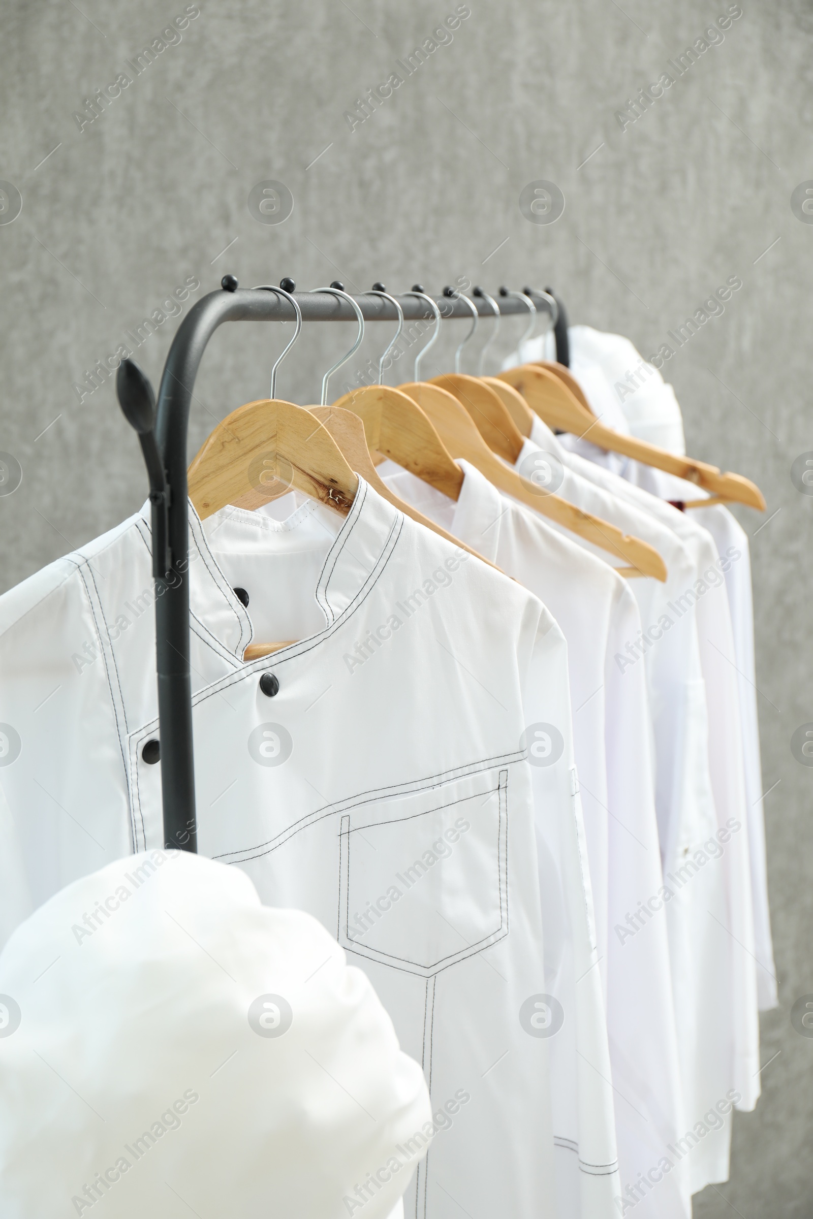 Photo of Chefs' uniforms on clothing rack against grey background, closeup