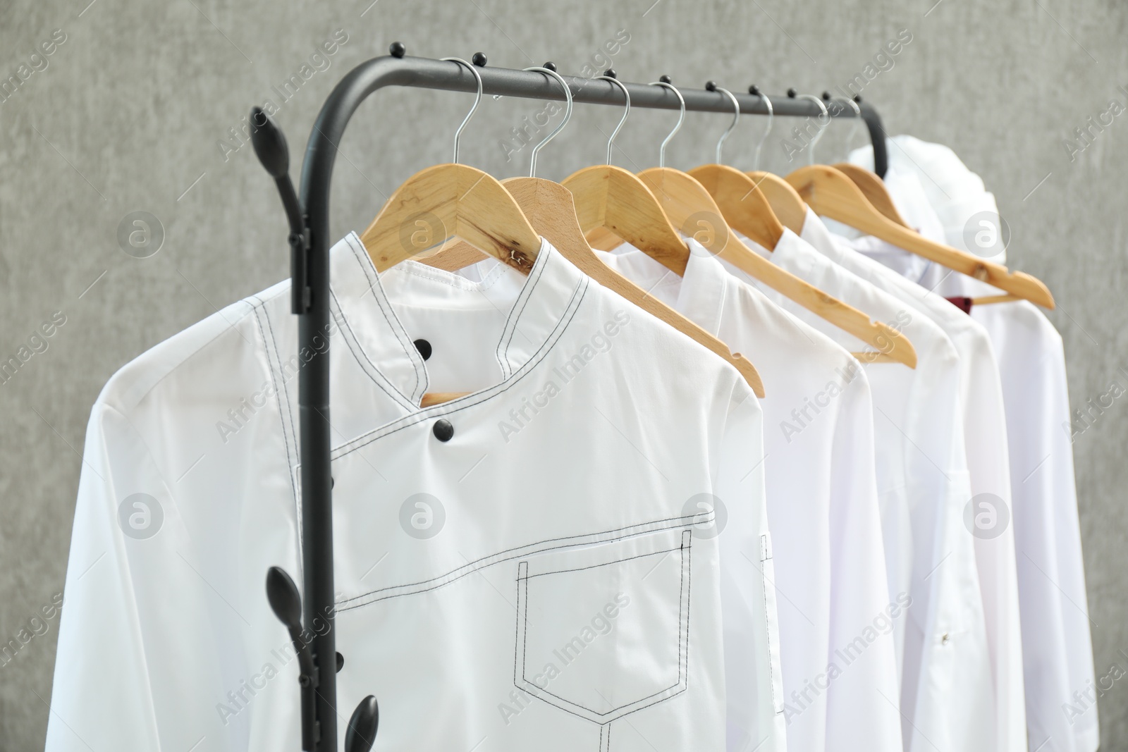 Photo of Chefs' uniforms on clothing rack against grey background, closeup