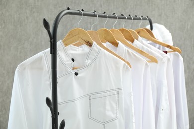 Chefs' uniforms on clothing rack against grey background, closeup