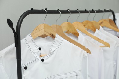 Chefs' uniforms on clothing rack against grey background, closeup