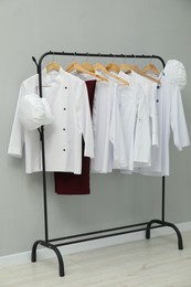 Photo of Chefs' uniforms on clothing rack near grey wall indoors