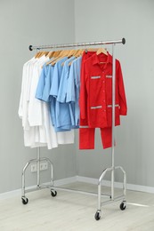 Photo of Different medical workers' uniforms on clothing rack near grey wall indoors