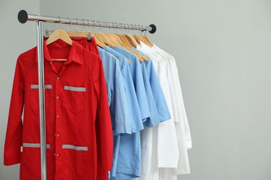 Photo of Different medical workers' uniforms on clothing rack against grey background. Space for text