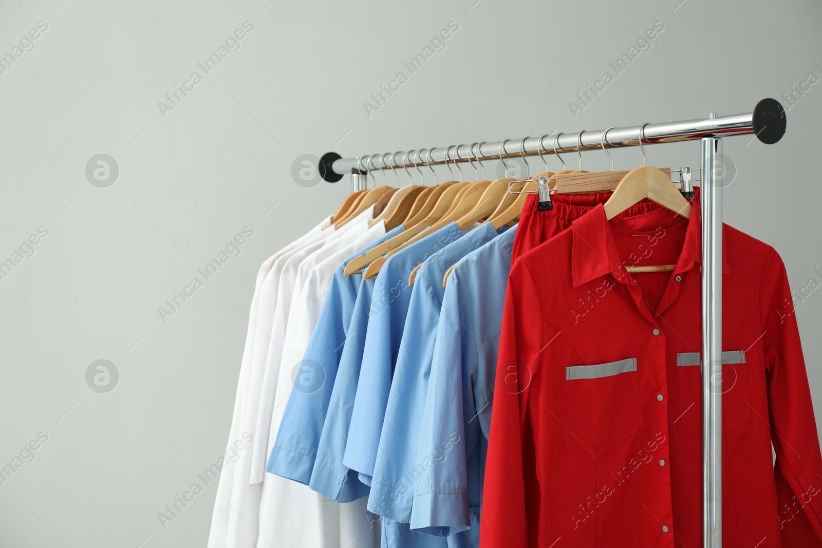 Photo of Different medical workers' uniforms on clothing rack against grey background. Space for text