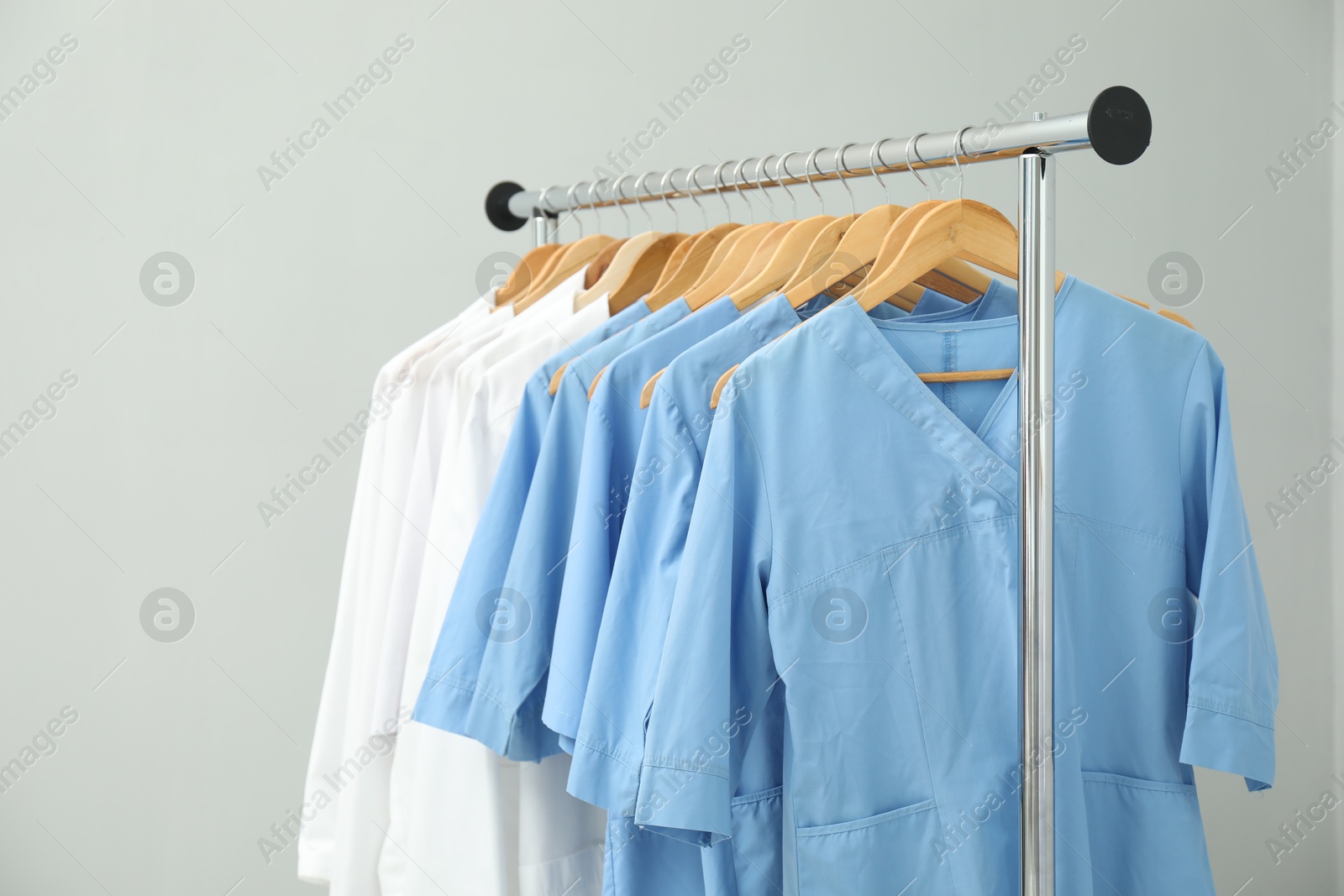 Photo of Different medical workers' uniforms on clothing rack against grey background