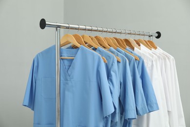 Photo of Different medical workers' uniforms on clothing rack against grey background