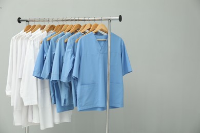 Photo of Different medical workers' uniforms on clothing rack against grey background. Space for text