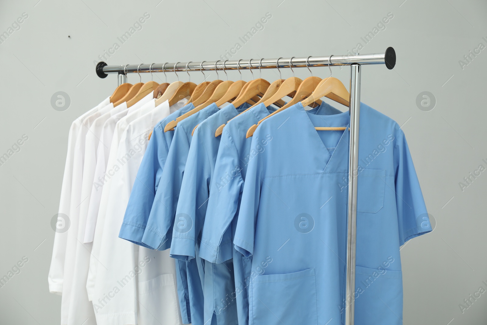 Photo of Different medical workers' uniforms on clothing rack against grey background