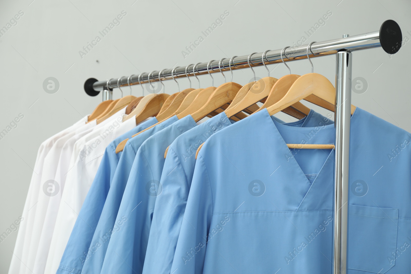 Photo of Different medical workers' uniforms on clothing rack against grey background