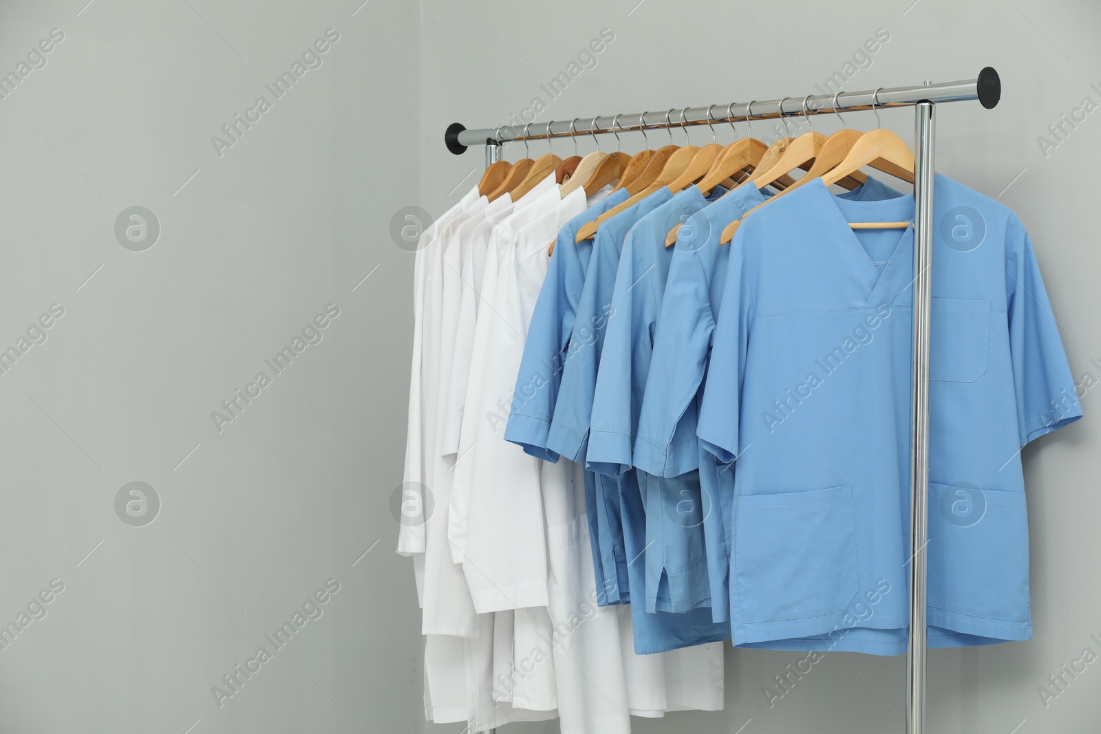 Photo of Different medical workers' uniforms on clothing rack against grey background. Space for text