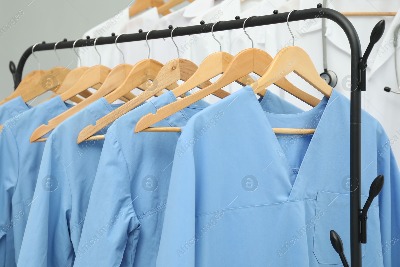 Photo of Different medical workers' uniforms on clothing racks against grey background, closeup