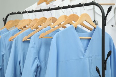 Different medical workers' uniforms on clothing racks against grey background, closeup