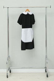 Maid's uniform on clothing rack near grey wall indoors