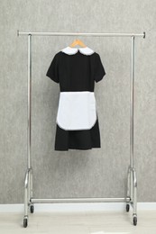 Maid's uniform on clothing rack near grey wall indoors