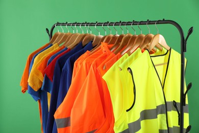 Different workers' uniforms and reflective vests on clothing rack against green background