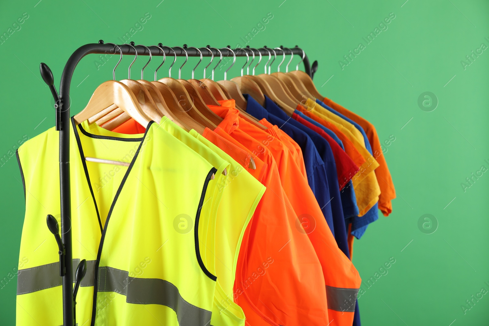 Photo of Different workers' uniforms and reflective vests on clothing rack against green background