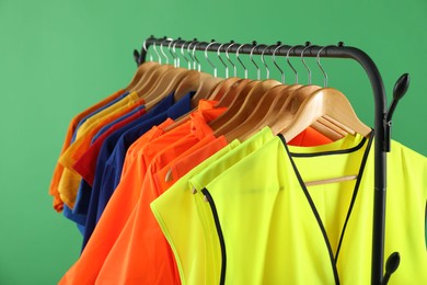 Photo of Different workers' uniforms and reflective vests on clothing rack against green background