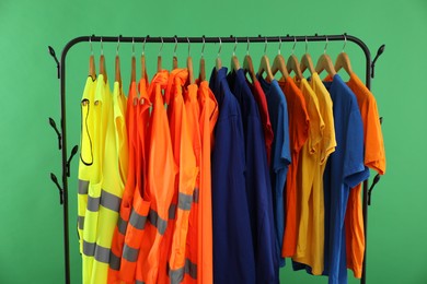 Photo of Different workers' uniforms and reflective vests on clothing rack against green background