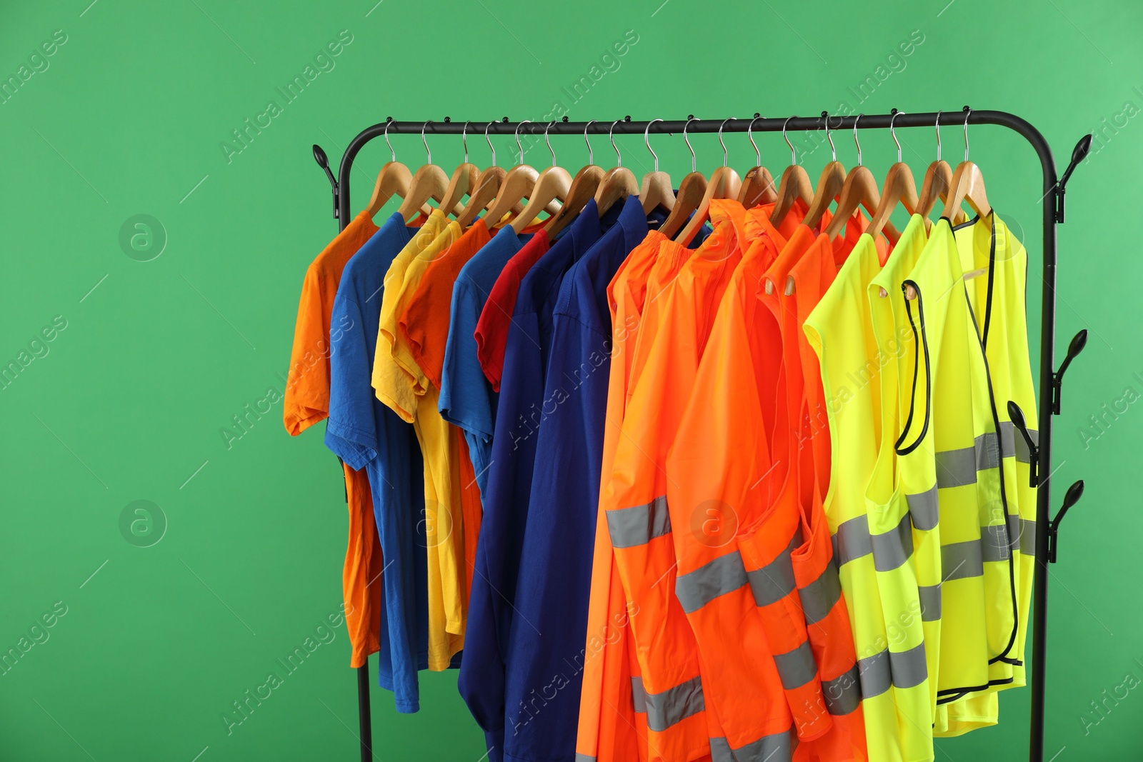 Photo of Different workers' uniforms and reflective vests on clothing rack against green background