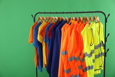 Different workers' uniforms and reflective vests on clothing rack against green background