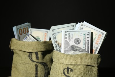 Photo of Dollar banknotes in sacks against black background, closeup