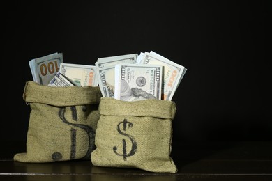 Photo of Dollar banknotes in sacks on wooden table against black background, space for text