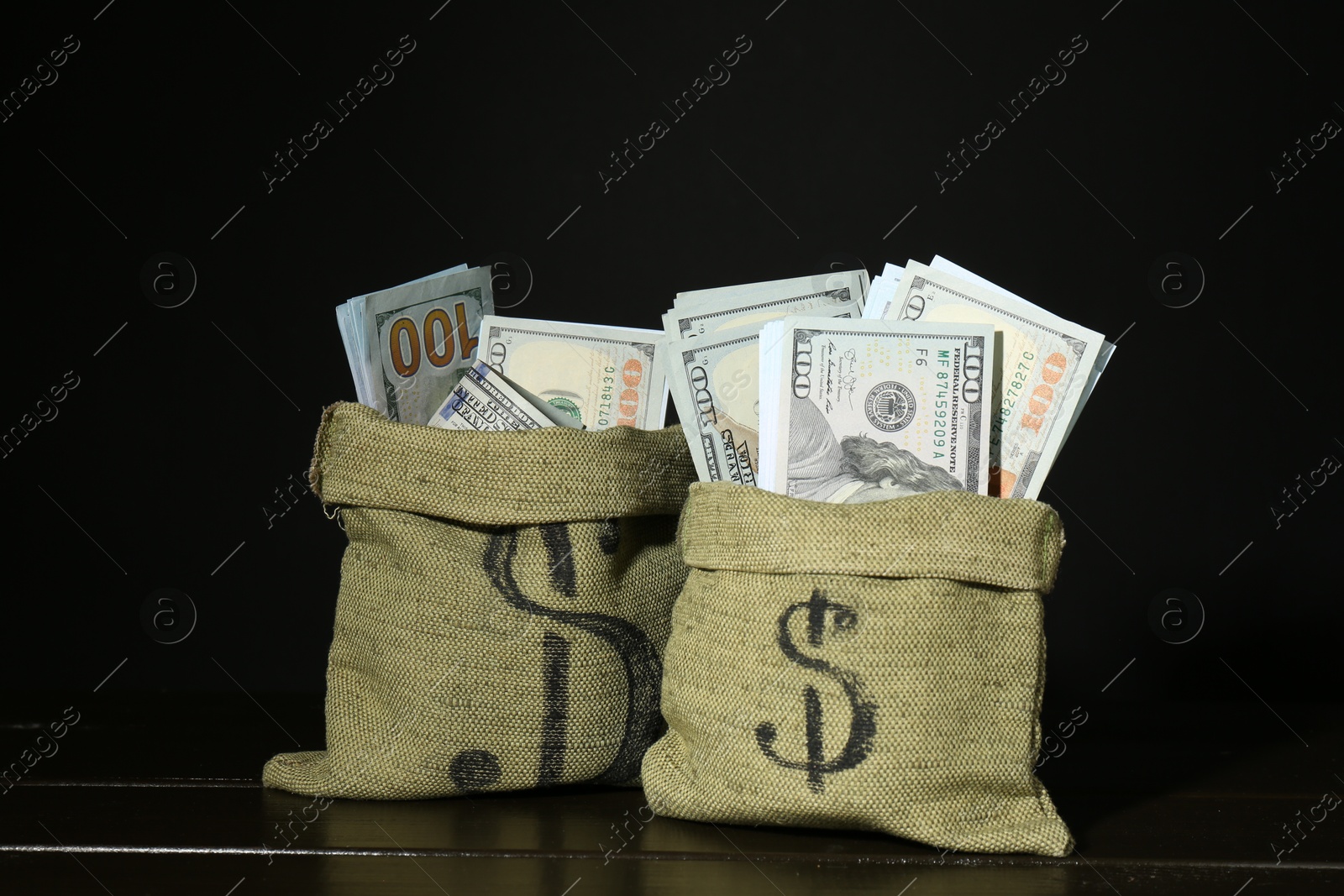 Photo of Dollar banknotes in sacks on wooden table against black background