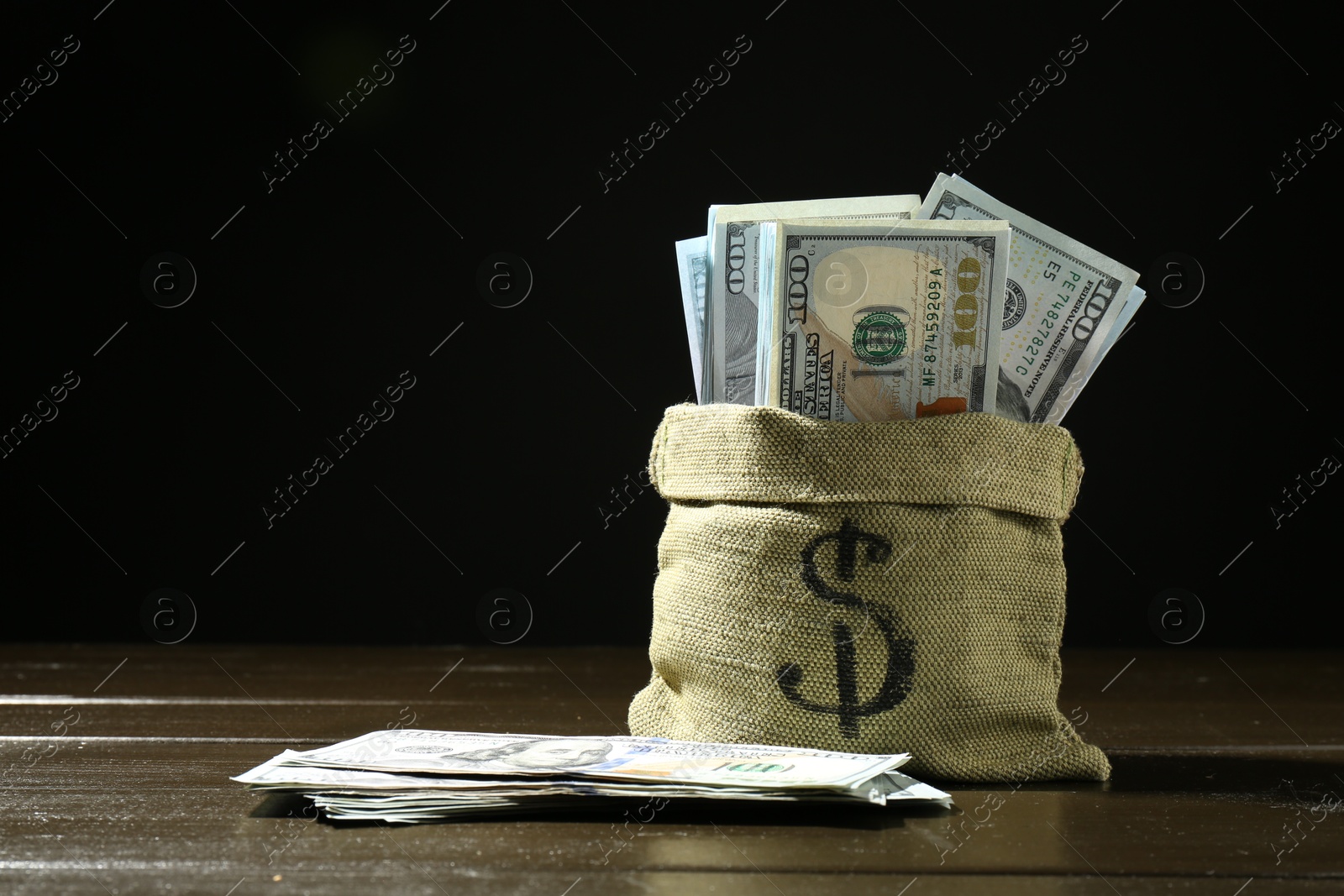 Photo of Dollar banknotes in sack on wooden table against dark background