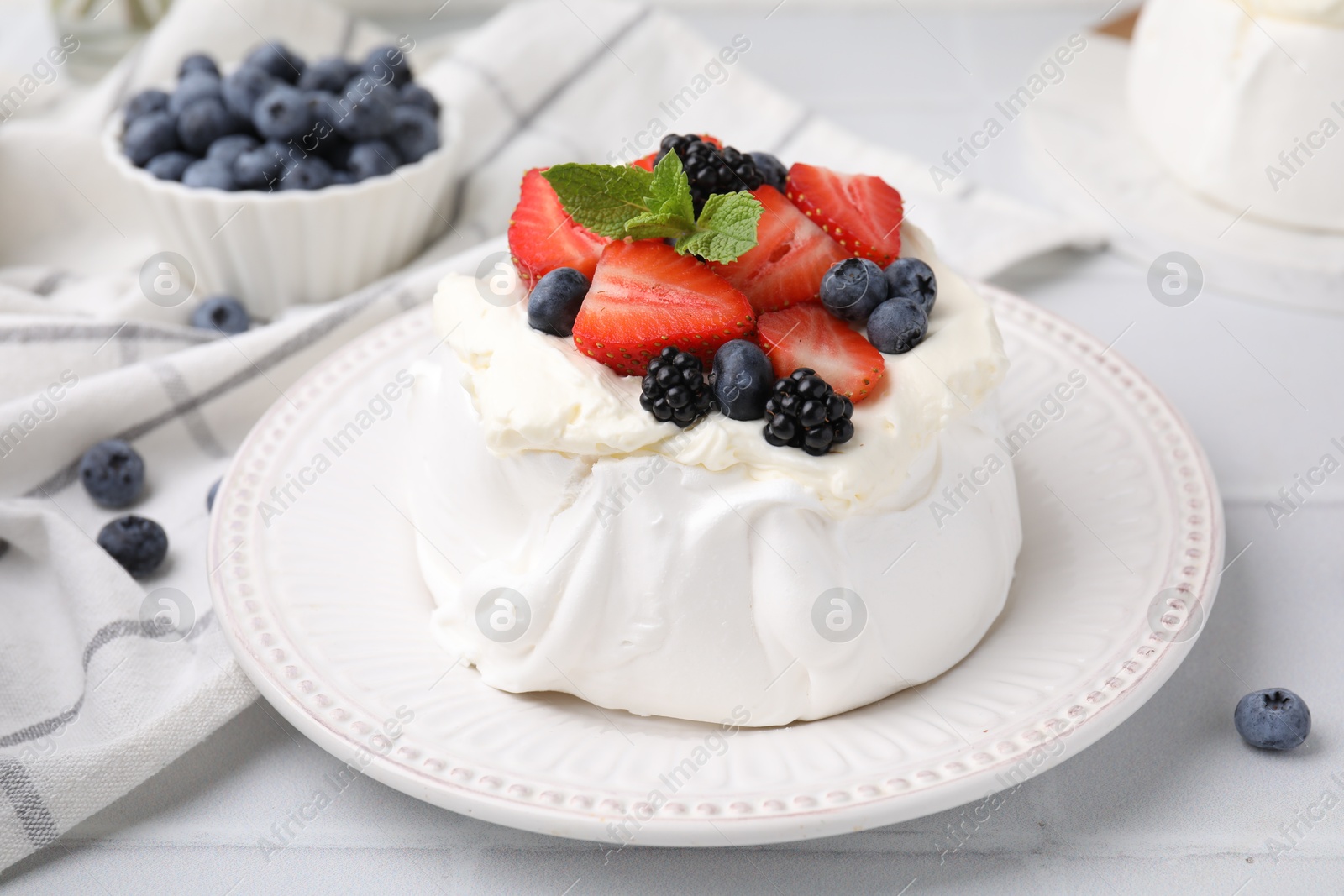 Photo of Pavlova cake (meringue dessert) with whipped cream, fresh berries and mint on white table, closeup