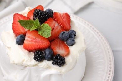 Photo of Pavlova cake (meringue dessert) with whipped cream, fresh berries and mint on white table, closeup