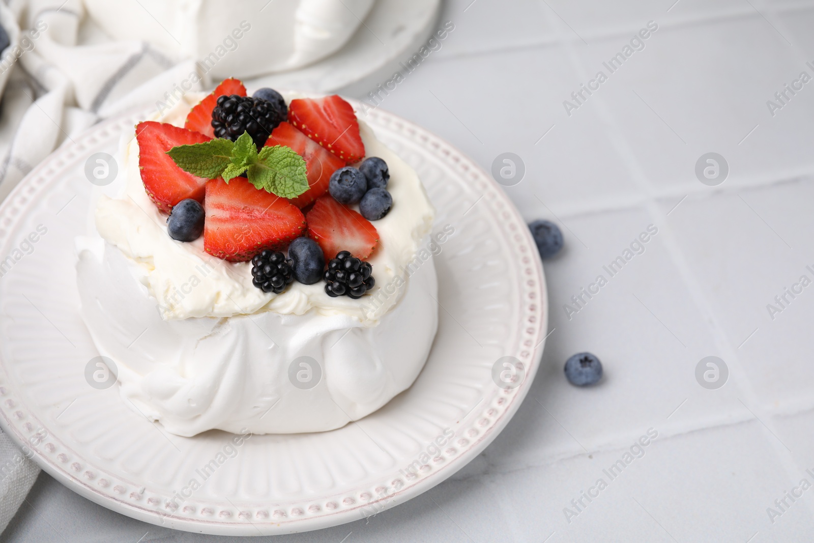 Photo of Pavlova cake (meringue dessert) with whipped cream, fresh berries and mint on white tiled table, closeup