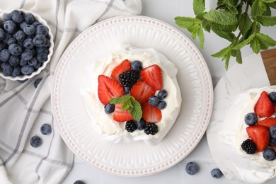 Photo of Pavlova cake (meringue dessert) with whipped cream, fresh berries and mint on white table, flat lay