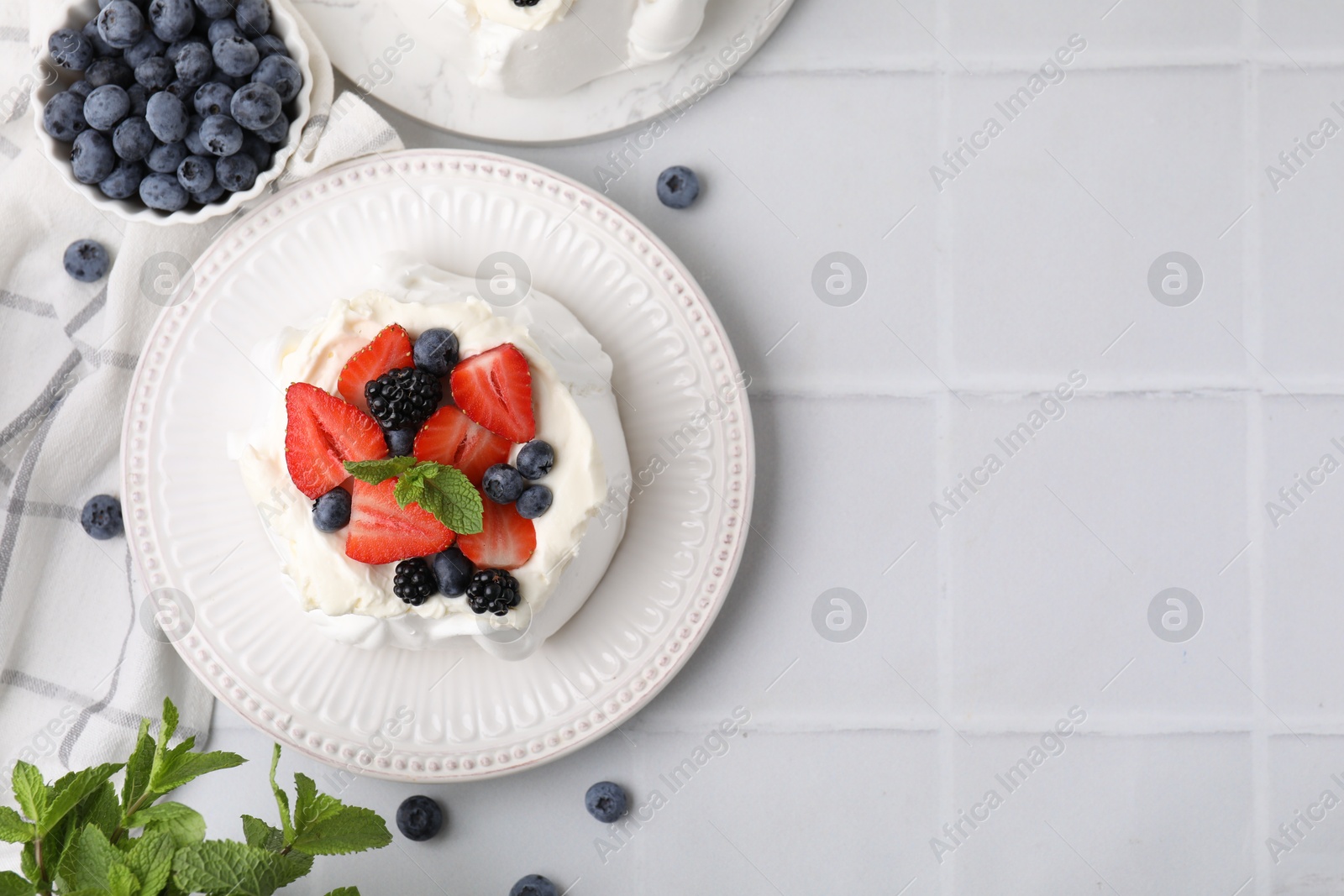 Photo of Pavlova cake (meringue dessert) with whipped cream, fresh berries and mint on white tiled table, flat lay. Space for text