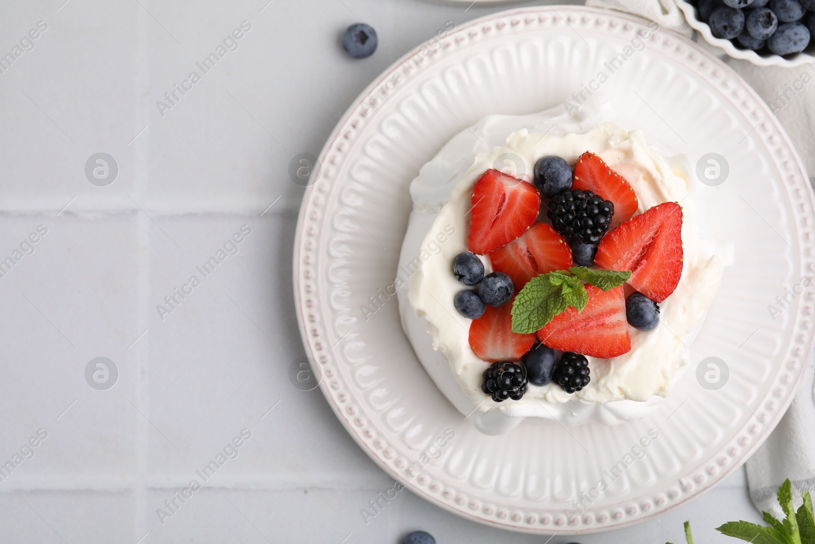 Photo of Pavlova cake (meringue dessert) with whipped cream, fresh berries and mint on white tiled table, top view. Space for text